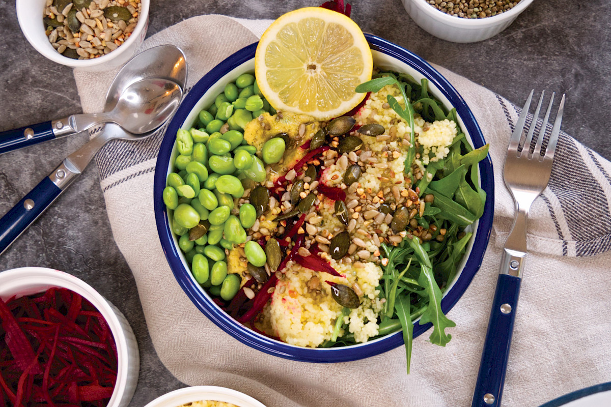 Eine klassische Bowl auf Rucolabasis mit Couscous und Hummus.